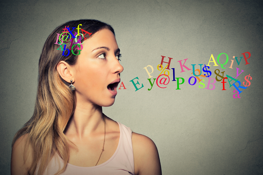 Side view portrait woman talking with alphabet letters in her head and coming out of her open mouth isolated grey wall background. Human face expressions, emotions. Communication, intelligence concept